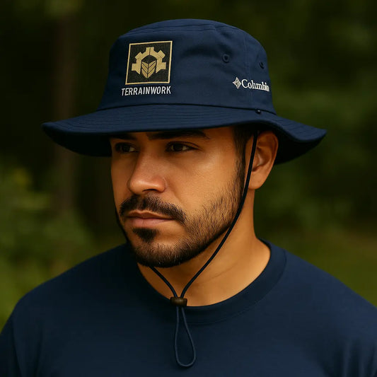 Bearded man wearing a collegiate navy Columbia Booney hat standing near construction site under bright daylight.